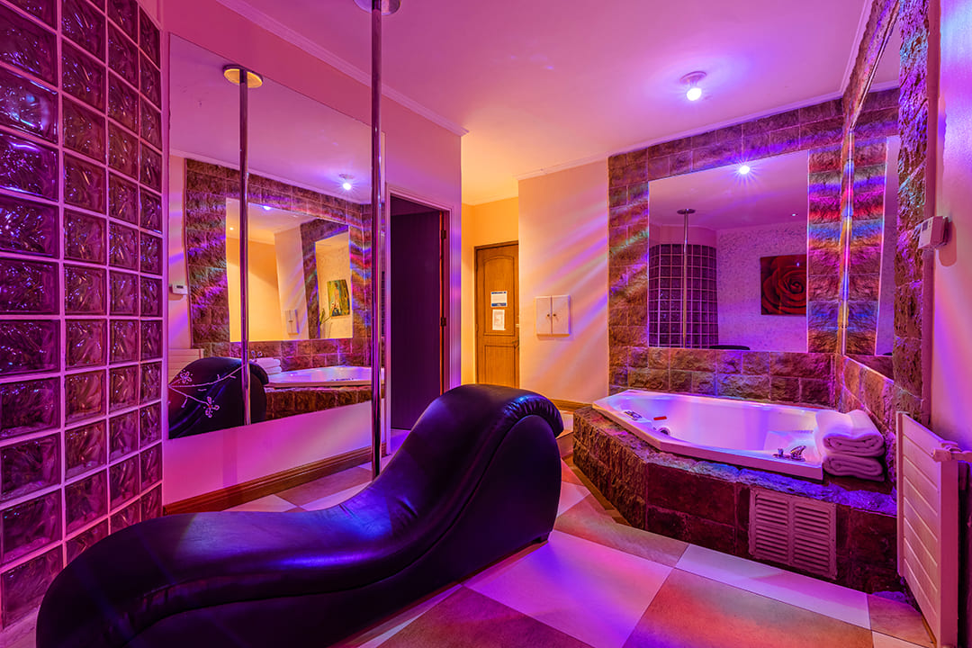 Habitación acogedora decorada en tonos morados, cuenta con una barra de pole dance, sillón del amor y un jacuzzi.